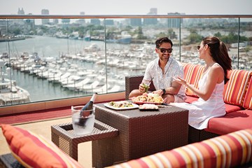 Man and woman enjoying some food and drinks while lounging at H2O at Golden Nugget with marina in view.